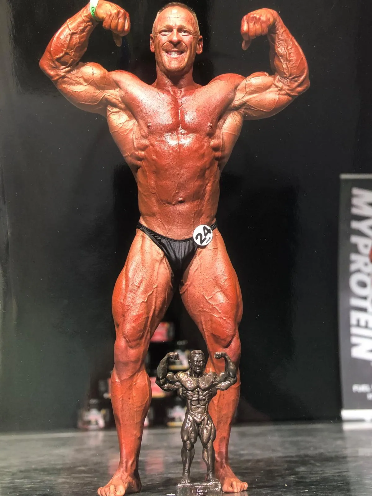 Garth Betteley posing on stage with a bodybuilding trophy